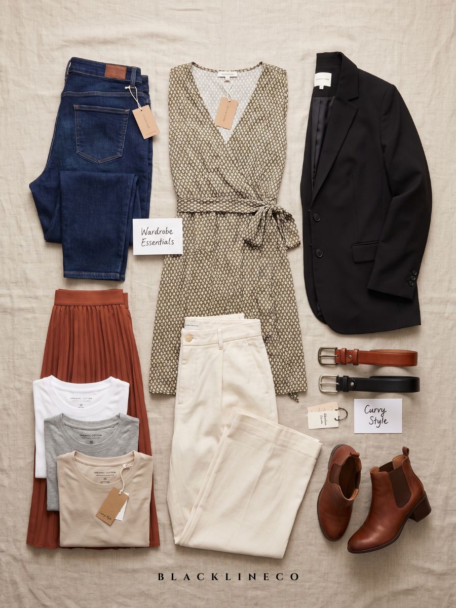 Flat lay of plus size capsule wardrobe essentials including jeans, blazer, wrap dress, and boots
